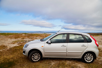 Fototapeta na wymiar Car on the beach of sea, river or lake with rocks on a cloudy day. The fjord of Northern Norway