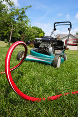 Fototapeta premium Lawnmower in backyard with red hose on grass in front