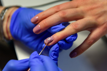 Obraz na płótnie Canvas Covering the nails with gel polish, drawing picture on the nail plate. Manicurist in blue gloves apply varnish with a thin brush. Manicure in pastel colors.