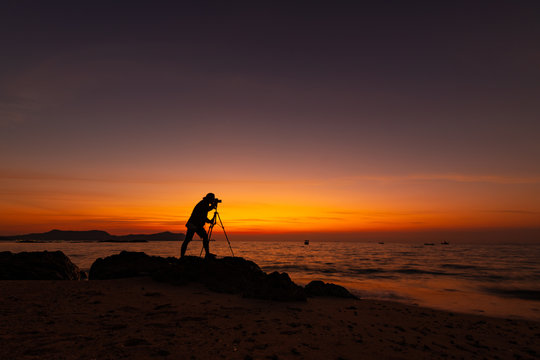 Silhouette of photographer or traveler taking a photograph sunset view landscape on top of stone with sunset twilight sky background.