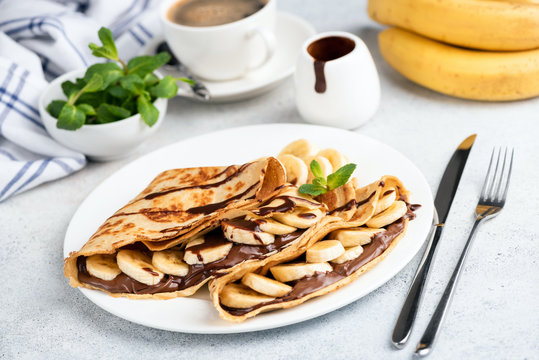 French crepes with chocolate spread and banana on white plate. Sweet food