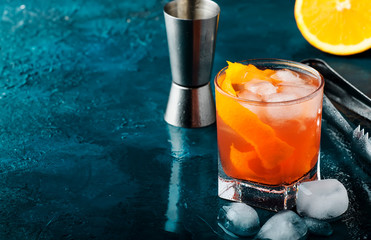 Orange Alcohol cocktail with red vermouth, bitter, soda, orange zest and ice, dark wooden bar...