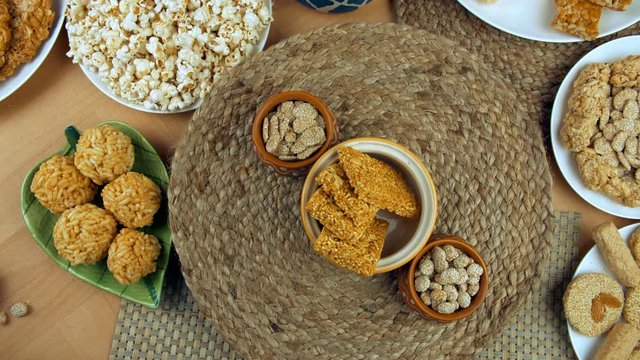 Zoom out shot of beautifully plated Lohri items for Pujabi's Lohri festival in India. Top view shot of bhujia chikki and rewri bowls rotating on a turntable surrounded by gajak rolls  til patti  po...