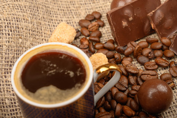 A Cup of coffee, coffee beans and pieces of brown sugar on a background of rough homespun fabric. Close up.