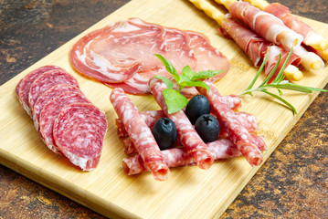 Meat and cheese plate antipasti snack with Prosciutto ham, Parmesan, Blue cheese, Cantaloupe melon and Olives on olive wood serving board on dark stone background