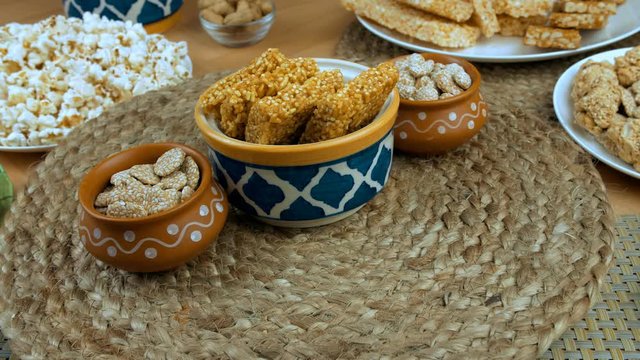 Pan shot of beautifully plated Lohri items consumed during the winter season in India. Closeup shot of bhujia chikki and rewari rotating on a turntable surrounded by til patti  gajak rolls  murmura...