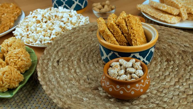 Closeup shot of delicious Lohri items served on Punjabi's Lohri festival in India. Still shot of bhujia chikki and rewri bowls rotating on a turntable surrounded by popcorns  murmura ladoo  murmura...