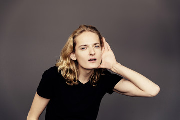 Attractive guy with long blonde hair, substituting a hand to his ear, eavesdrops with an interested...
