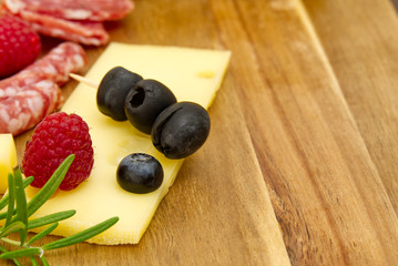 Meat and cheese plate antipasti snack with Prosciutto ham, Parmesan, Blue cheese, Cantaloupe melon and Olives on olive wood serving board on dark stone background