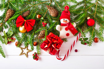 Christmas wooden background with fir tree decoration, cones and red berries, snowman, candy cane and present box.