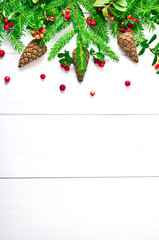 Christmas greeting card. Text space. Christmas fir tree, cones and red berries of cranberry on a white wooden background.  Top view.