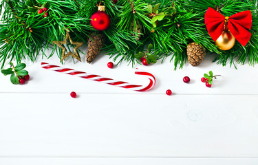 Fototapeta na wymiar Christmas pine tree with decoration, red berries, balls, candy cane, cones on a white wooden background. Christmas greeting card. Text space.