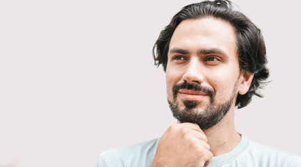 Portrait of a handsome young latin man, swarthy brunette with a beard and dark eyes on a gray background. Face head close up