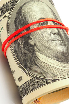 A bundle of old-style 100 dollar bills lies on a white paper background. Banknotes are rolled up and pulled together with an elastic band. Money under the table. Vertical shot. Not isolated. Macro