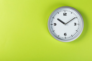 White wall clock with a yellow used hanging on the wall. Minimalist image of a wall clock on a green background with copy space