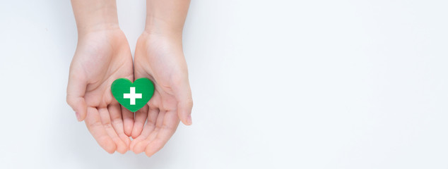 Hands holding a beautiful green heart with hospital white cross symbol on it showing a concept of Health care service, cancer treatment and heart surgery. Banner top view Isolated on white background.