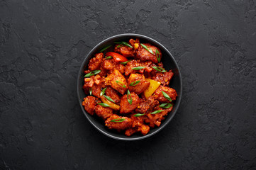Fish Manchurian dry looks like Schezwan Fish in black bowl at dark slate background. Fish Manchurian - is indo chinese cuisine dish with deep fried salmon, bell peppers, sauce and onion. Top view - obrazy, fototapety, plakaty