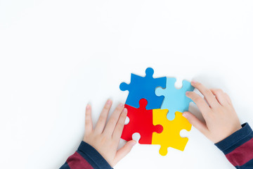 Top view, hands of an autistic child play colorful puzzle which is a symbol of public awareness for autism spectrum disorder - World Autism Awareness day on April 2, Understanding and Acceptance. - obrazy, fototapety, plakaty