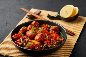 Fish Manchurian dry looks like Schezwan Fish in black bowl at dark slate background. Fish Manchurian - is indo chinese cuisine dish with deep fried salmon, bell peppers, sauce and onion.