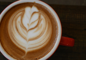 Closed up the cappuccino in red coffee cup on wooden table
