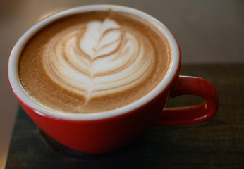 Closed up the cappuccino in red coffee cup on wooden table
