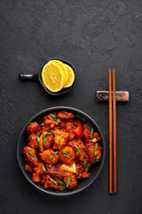 Fish Manchurian dry looks like Schezwan Fish in black bowl at dark slate background. Fish Manchurian - is indo chinese cuisine dish with deep fried salmon, bell peppers, sauce and onion. Top view