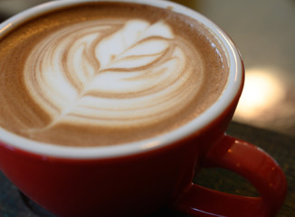 Closed up the cappuccino in red coffee cup on wooden table