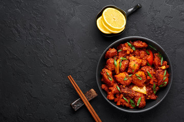 Fish Manchurian dry looks like Schezwan Fish in black bowl at dark slate background. Fish Manchurian - is indo chinese cuisine dish with deep fried salmon, bell peppers, sauce and onion. Top view
