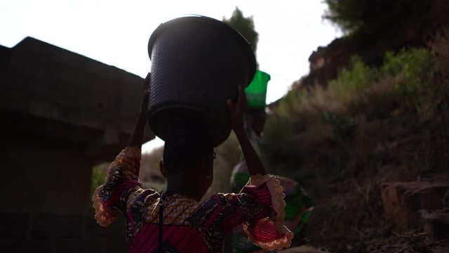Two Girls Climbing A Mountain Path Carrying Water Buckerts On Their head