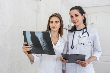 Doctor with intern examining patient's x-ray. Both wearing medical uniform and standing in hospital