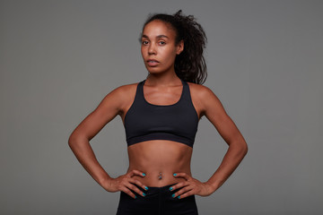 Studio shot of young pretty dark skinned curly lady with belly button piercing holding hands on her...