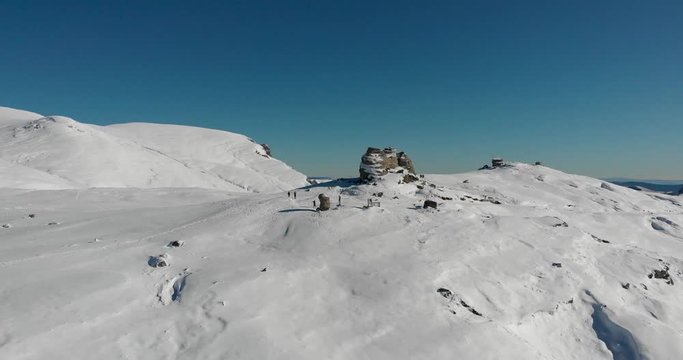 Aerial, drone shot towards people at the sphinx rock formation, on the top of the southern Carpathians, on a sunny winter day, in the Bucegi Natural Park, Romania
