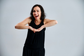 Portrait of a pretty brunette woman in a black dress on a white background. Shows emotions with hands in different poses right in front of the camera.