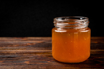  Honey in glass jar and fresh raspberry on dark wooden background.