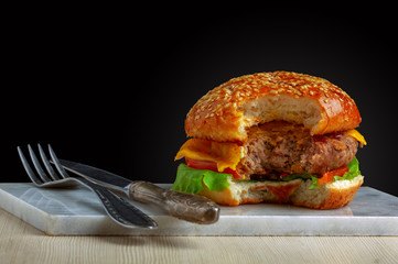Craft burger with fork and knife on black background. Cheeseburger on plate.