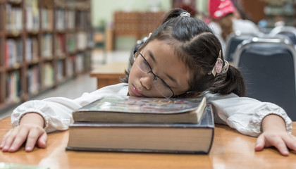 School student fall asleep while reading book in library or class from overwhelming learning or studying hard for exam, effecting kid health 