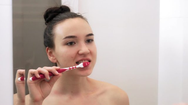 A young woman is brushing her teeth in the bathroom. Portrait in mirror image.