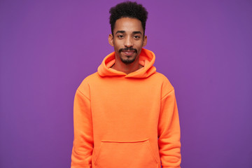 Studio shot of attractive young bearded dark skinned curly brunette male keeping lips folded while...