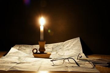 La cartina sulla tavola illuminata dalla fiamma della candela - obrazy, fototapety, plakaty