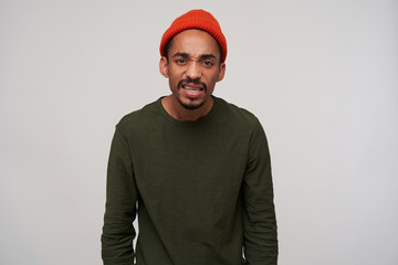 Displeased young attractive brown-eyed dark skinned brunette male with beard frownig his face and looking to camera with pout, isolated over white background