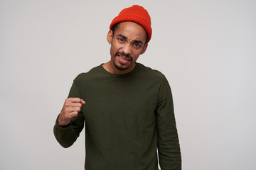 Portrait of young brown-eyed dark skinned brunette male with beard folding raised hand in fist and frowning his face while looking to camera, isolated over white background