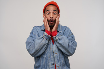 Shocked young handsome dark skinned brunette guy with beard holding face with palms and rounding...