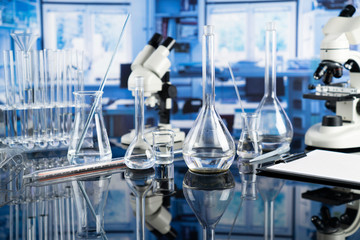 Modern scientific laboratory interior. Laboratory glassware and microscope on the glass table.