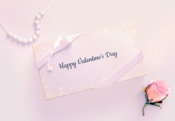 Valentine's day card with a ribbon, pearls and a rose on a pink background