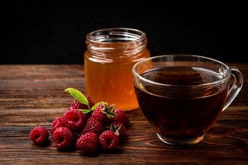 Cup of black tea with raspberry and honey on dark wooden background.