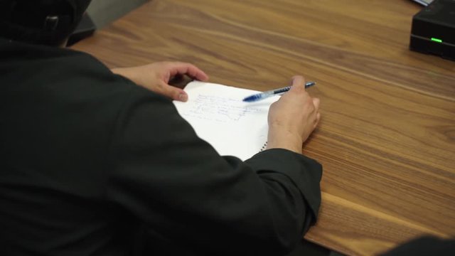 Mid shot of a person drawing on a piece of paper because he is bored in class.