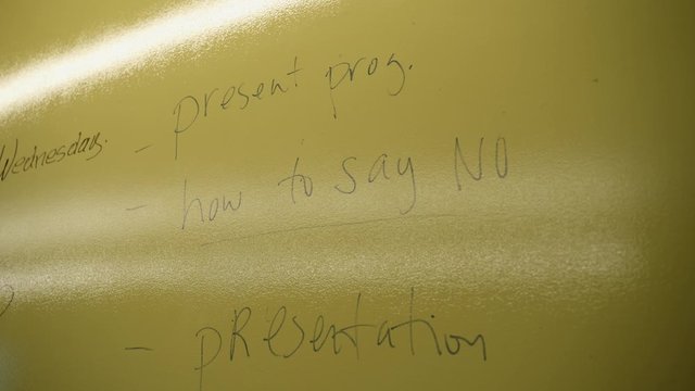Close up shot of a yellow board showing class in session. People are writing on the board to translate Spanish to English.