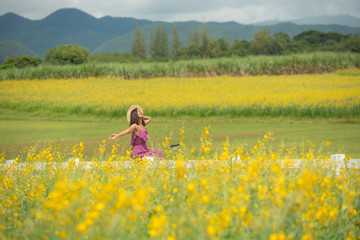 asia woman with a hat in her hand walks in a field with field flowers and smiles sincerely, happy...