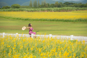 asia woman with a hat in her hand walks in a field with field flowers and smiles sincerely, happy...
