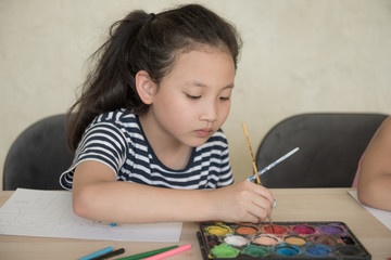 little girl with brush painting on table in School, education, cut girl painting in at her home. Selective focus and small depth of field, Painting with watercolor, drawing, Creativity concept.